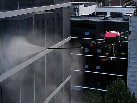 Dron de Dronex aplicando agua a presión sobre la fachada vidriada de un edificio en altura